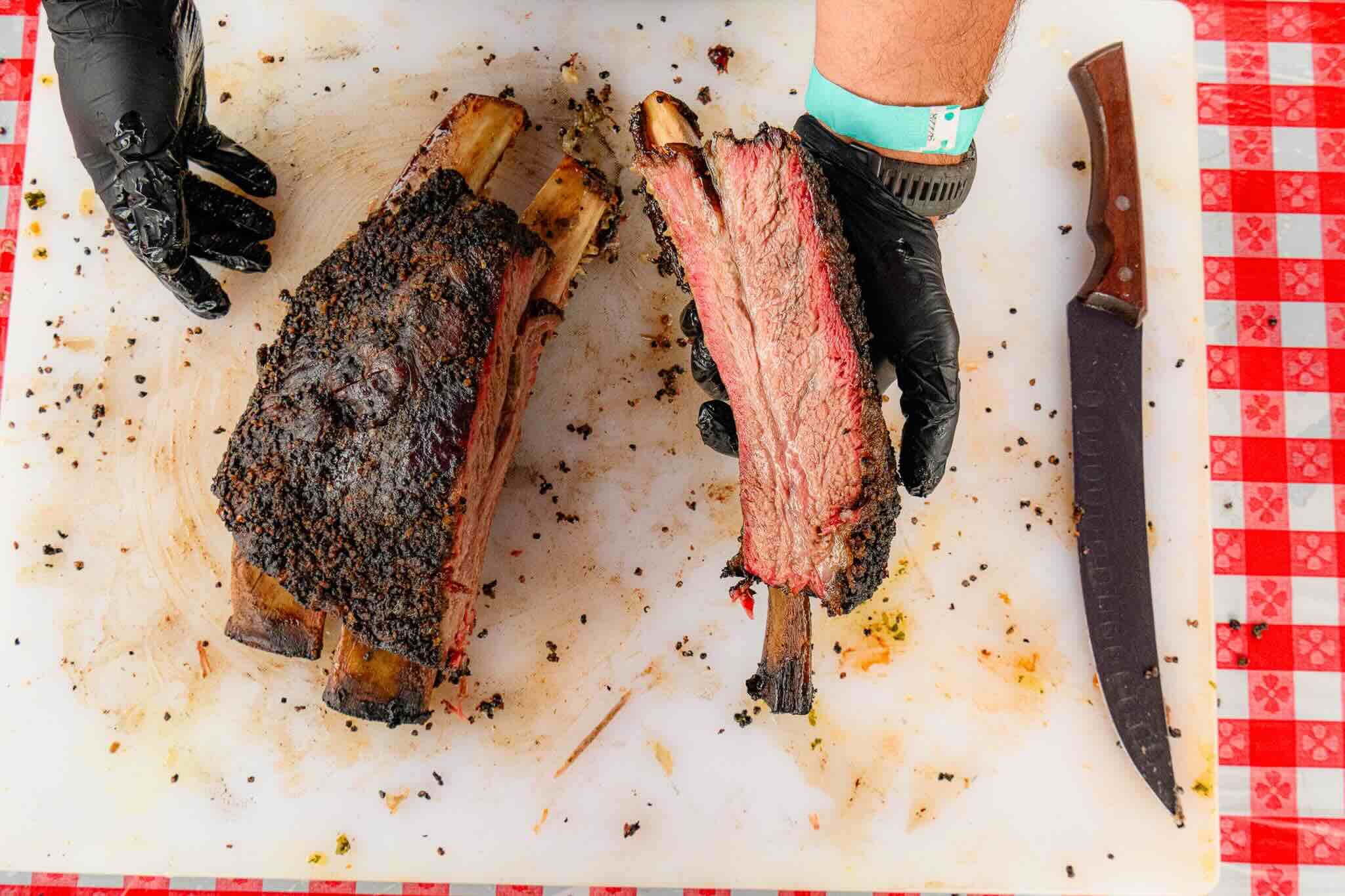 close up of a bbq smoker with its door open showing grill racks full or meats