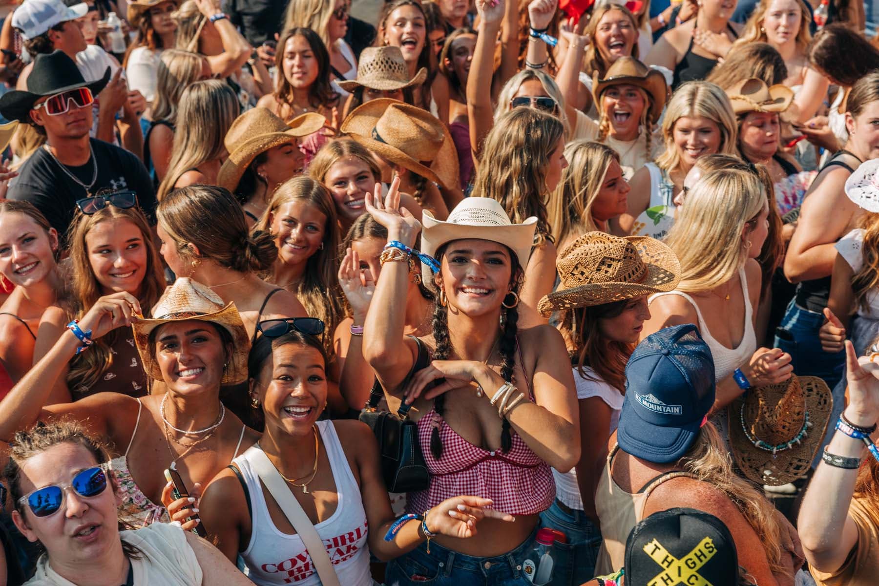 a large group of people with focus being a woman in a cowboy hat staring directly at the camera
