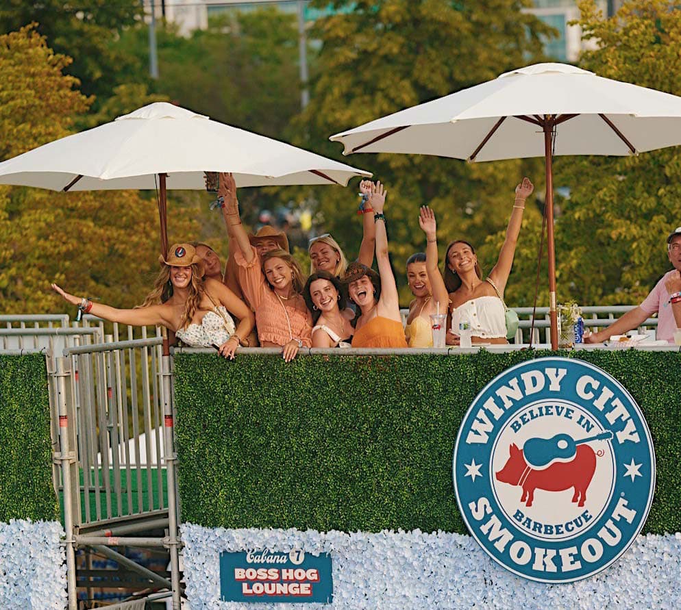 a group of concert goers waving to the camera from atop a concert cabana